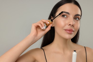 Photo of Beautiful young woman applying mascara on grey background