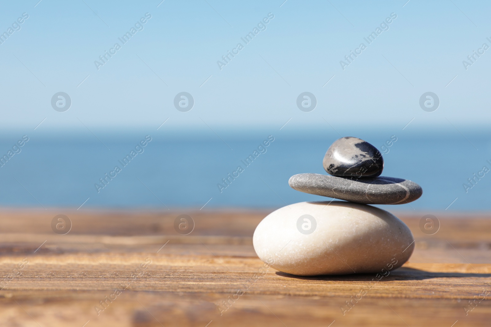 Photo of Stack of stones on wooden pier near sea, space for text. Zen concept