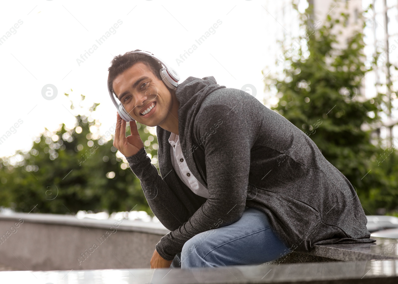 Photo of Handsome young African-American man with headphones listening to music on city street. Space for text