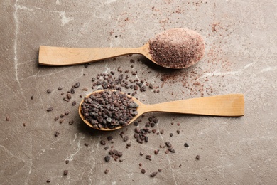Photo of Black salt in wooden spoons on grey table, flat lay