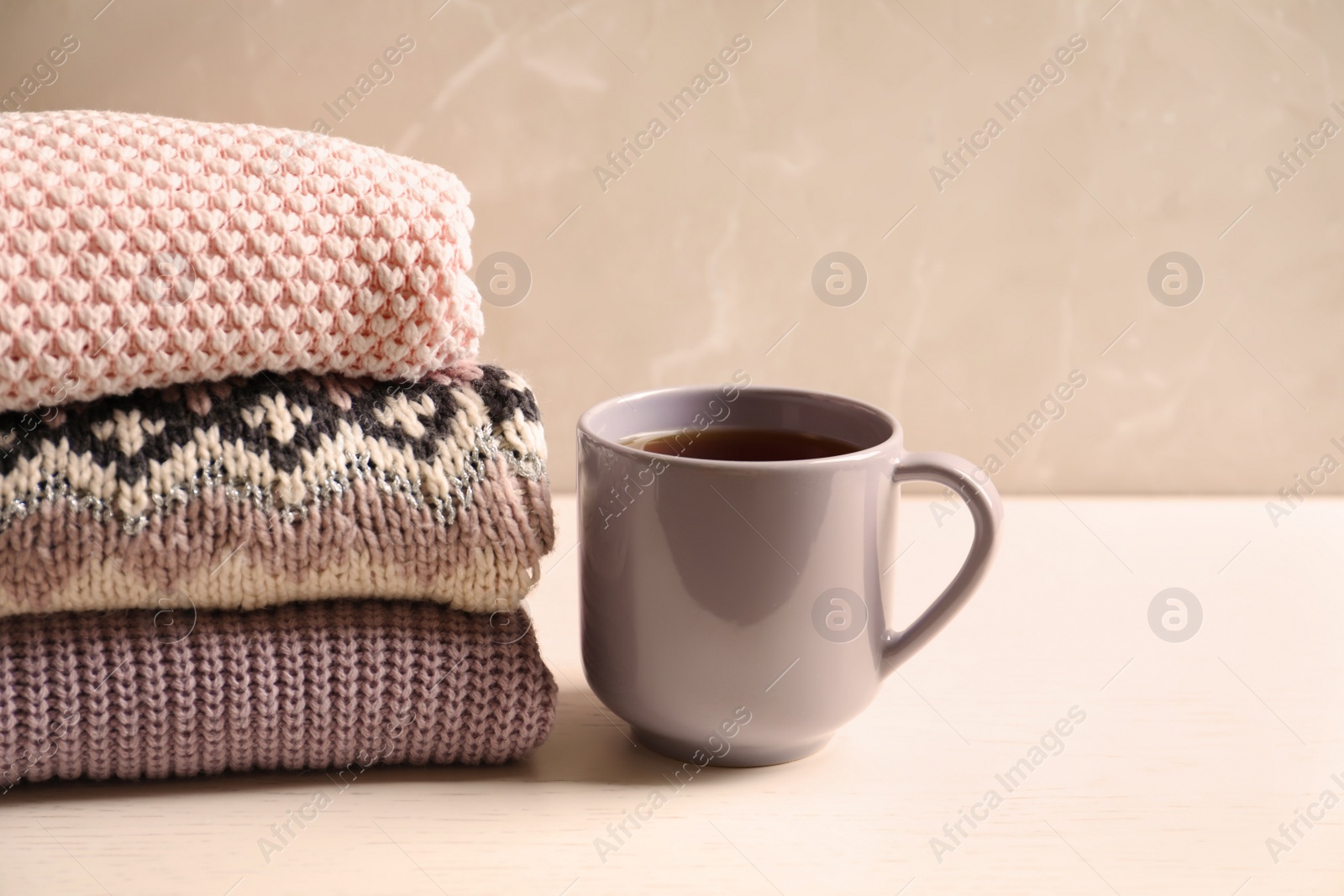 Photo of Stack of warm knitted clothes and cup of tea on table