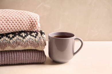 Photo of Stack of warm knitted clothes and cup of tea on table