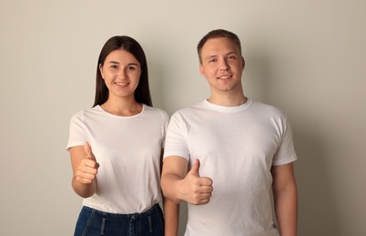 Photo of Portrait of happy young woman and man showing thumbs up on light background