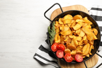 Photo of Dish of delicious oven baked potatoes with tomatoes and rosemary on white wooden background, top view. Space for text