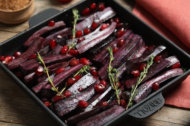 Photo of Raw cut black carrot with pomegranate seeds and thyme in baking dish on table, closeup