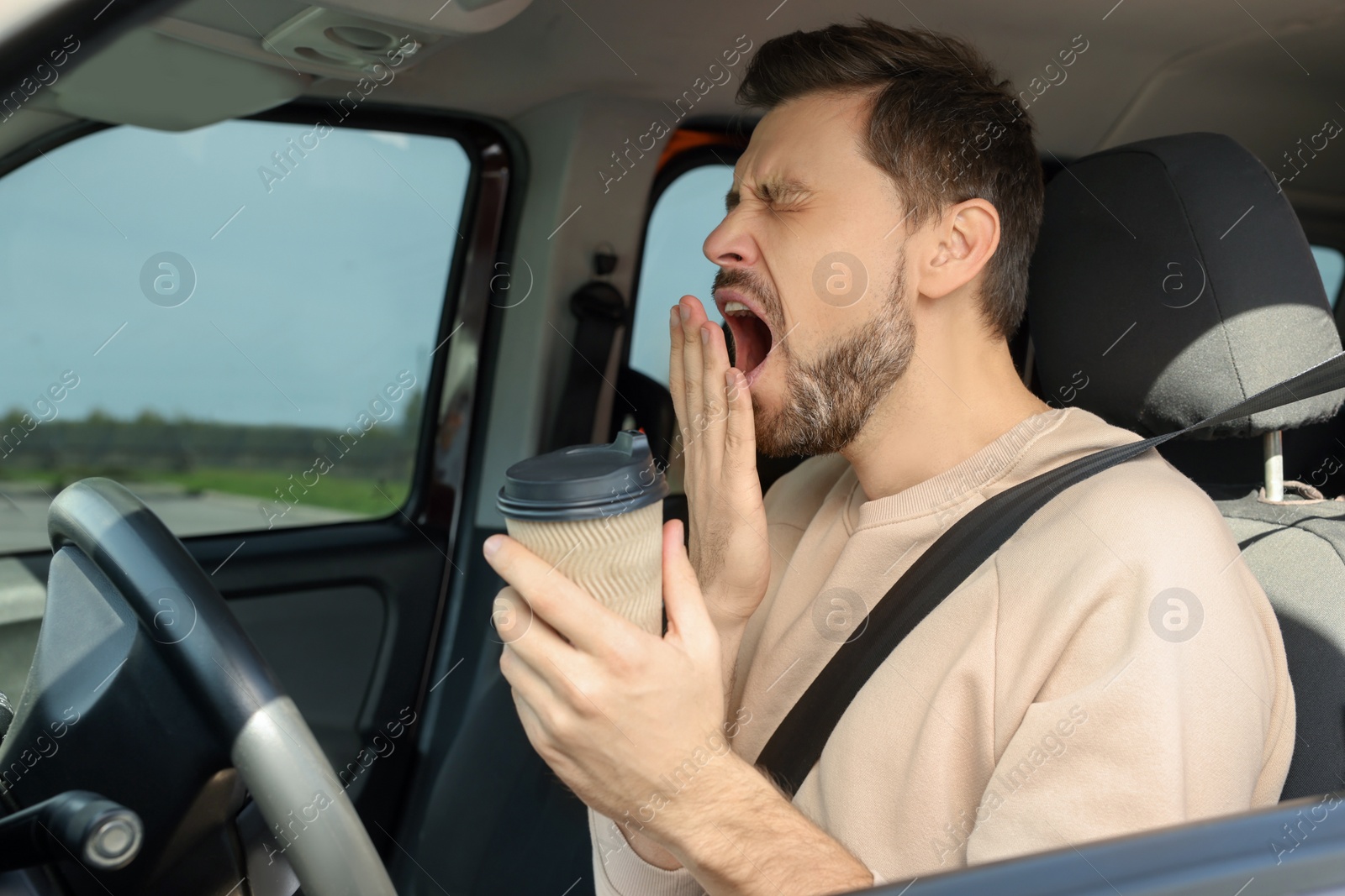 Photo of Sleepy man with cup of coffee yawning in modern car