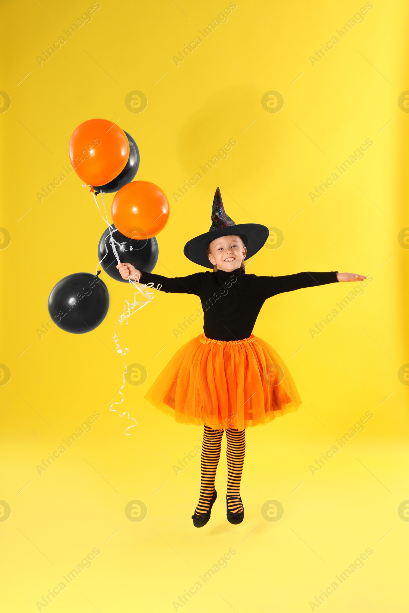 Photo of Cute little girl with balloons wearing Halloween costume on yellow background