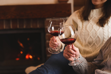Photo of Lovely couple with glasses of wine resting near fireplace at home, closeup. Winter vacation