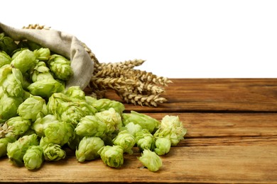 Overturned sack of hop flowers and wheat ears on wooden table against white background, space for text