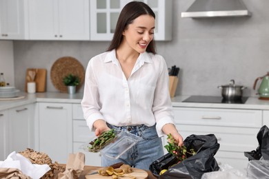 Photo of Garbage sorting. Woman putting food waste into plastic bag at table in kitchen