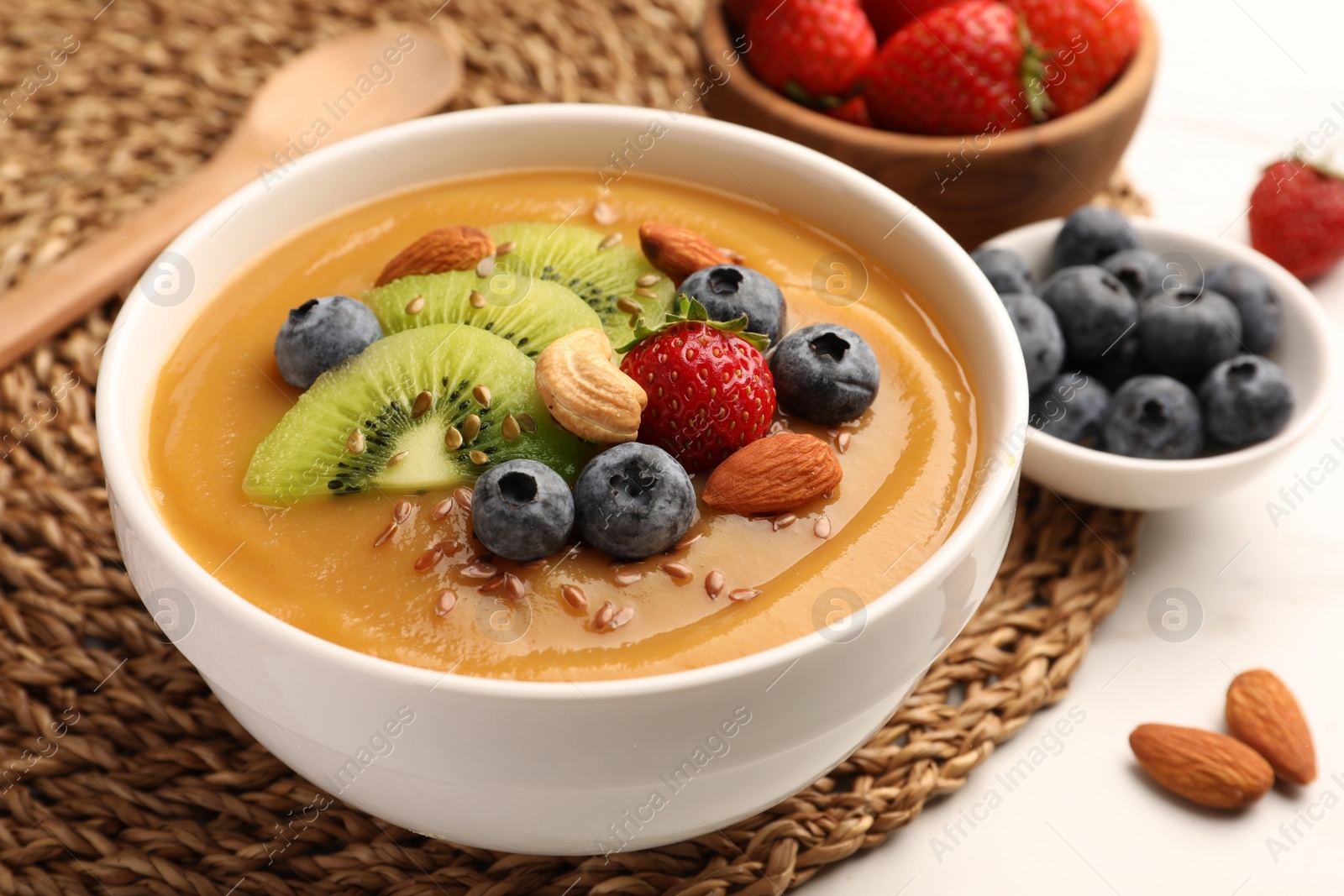 Photo of Delicious smoothie bowl with fresh berries, kiwi and nuts on table, closeup