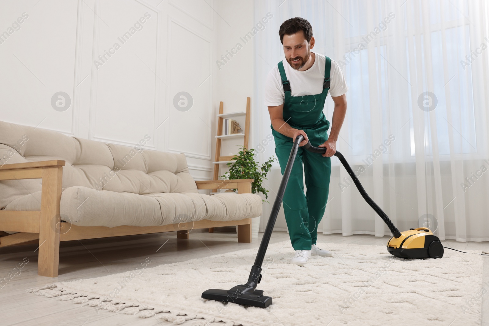 Photo of Dry cleaner's employee hoovering carpet with vacuum cleaner in room