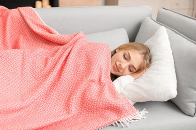 Beautiful young woman covered with plaid sleeping on sofa at home. Winter atmosphere