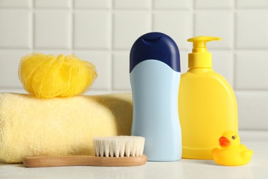 Photo of Baby cosmetic products, bath duck, brush and towel on white table against tiled wall