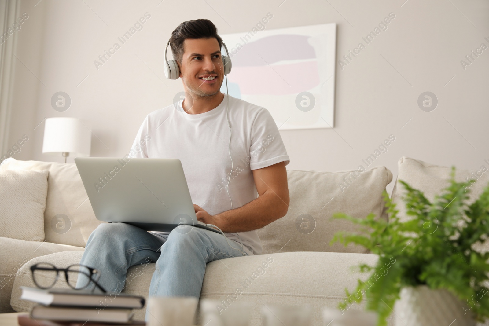 Photo of Man with laptop and headphones sitting on sofa at home