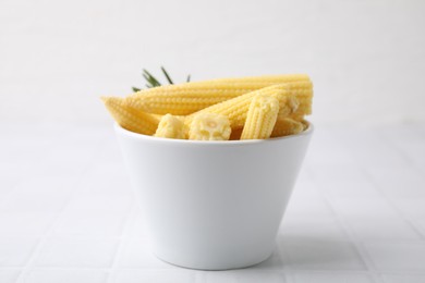 Photo of Tasty fresh yellow baby corns in bowl on white tiled table