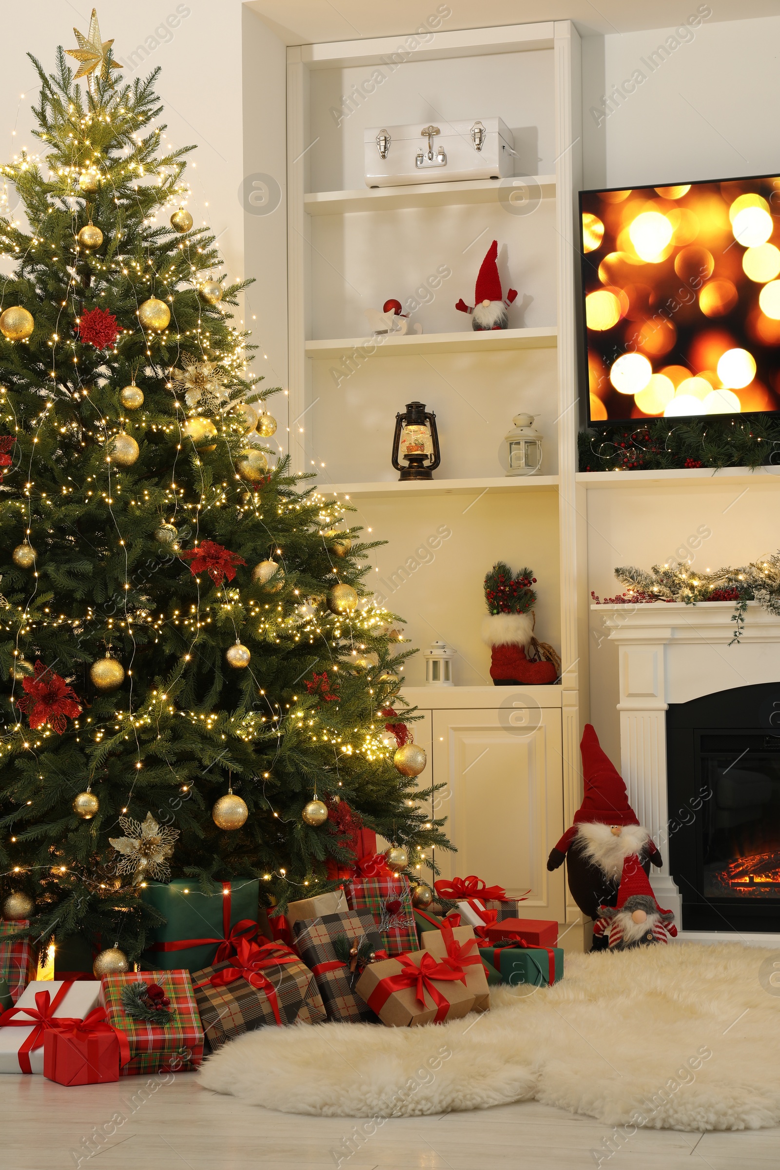 Photo of Many gift boxes under Christmas tree decorated with ornaments and festive lights in room