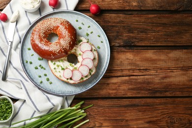 Photo of Delicious bagel with cream cheese, green onion and radish on wooden table, flat lay. Space for text