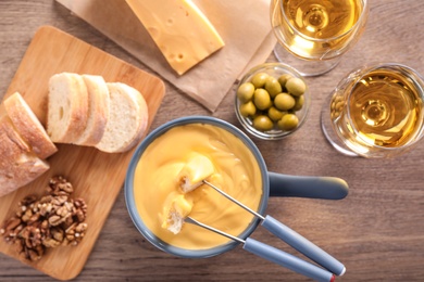 Photo of Flat lay composition with pot of cheese fondue and wine on wooden table