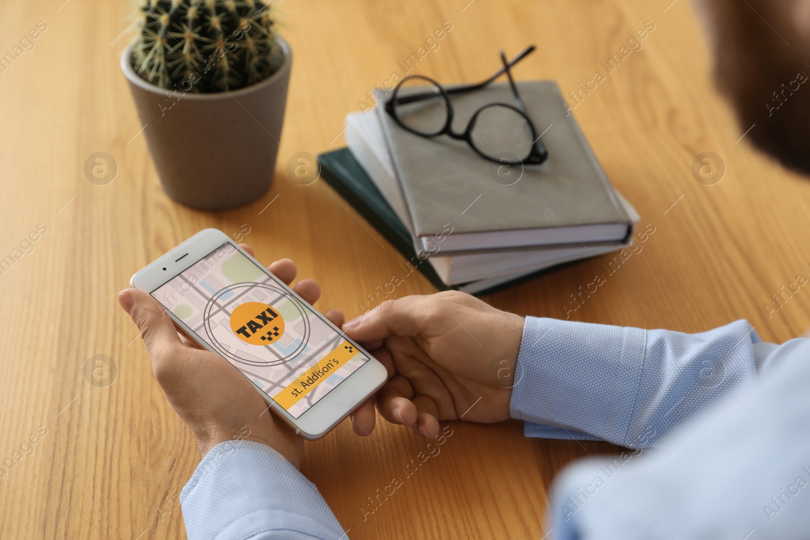 Photo of Man ordering taxi with smartphone at wooden table, closeup