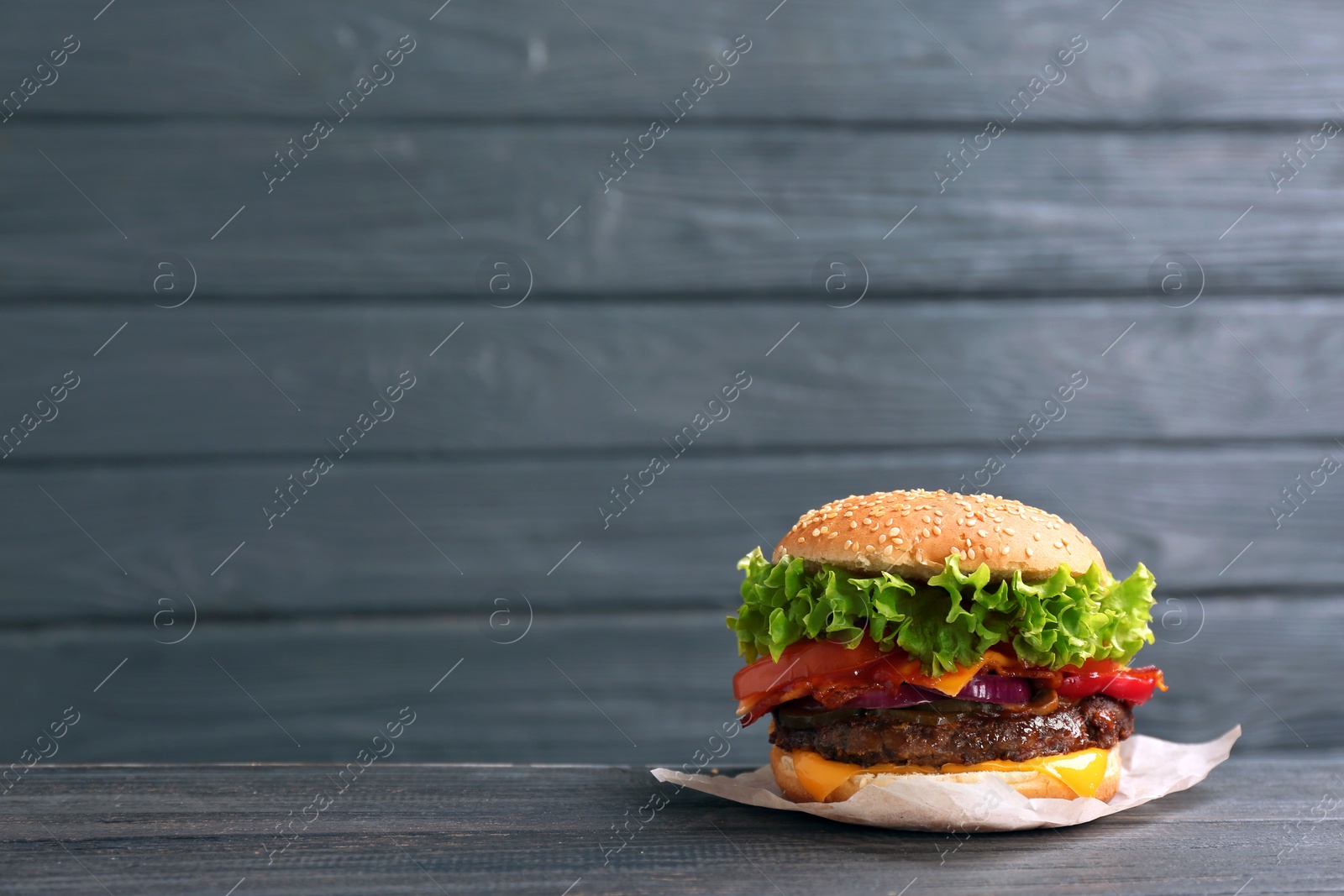 Photo of Tasty burger with bacon on table against wooden background. Space for text