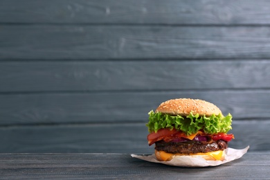 Photo of Tasty burger with bacon on table against wooden background. Space for text