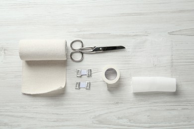 Photo of Medical bandage rolls, sticking plaster and scissors on white wooden table, flat lay