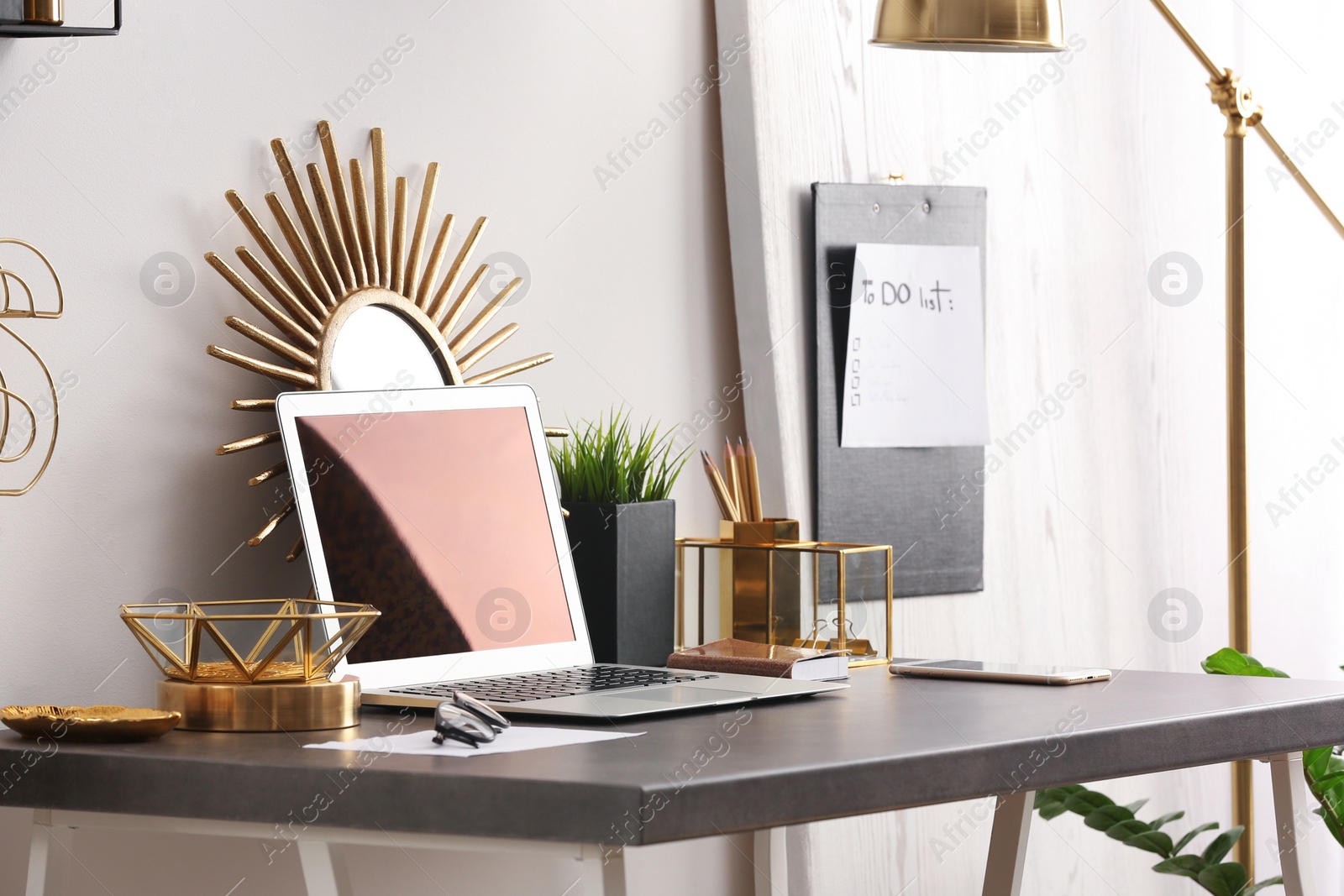 Photo of Modern workplace with laptop and golden decor on desk near wall. Stylish interior design