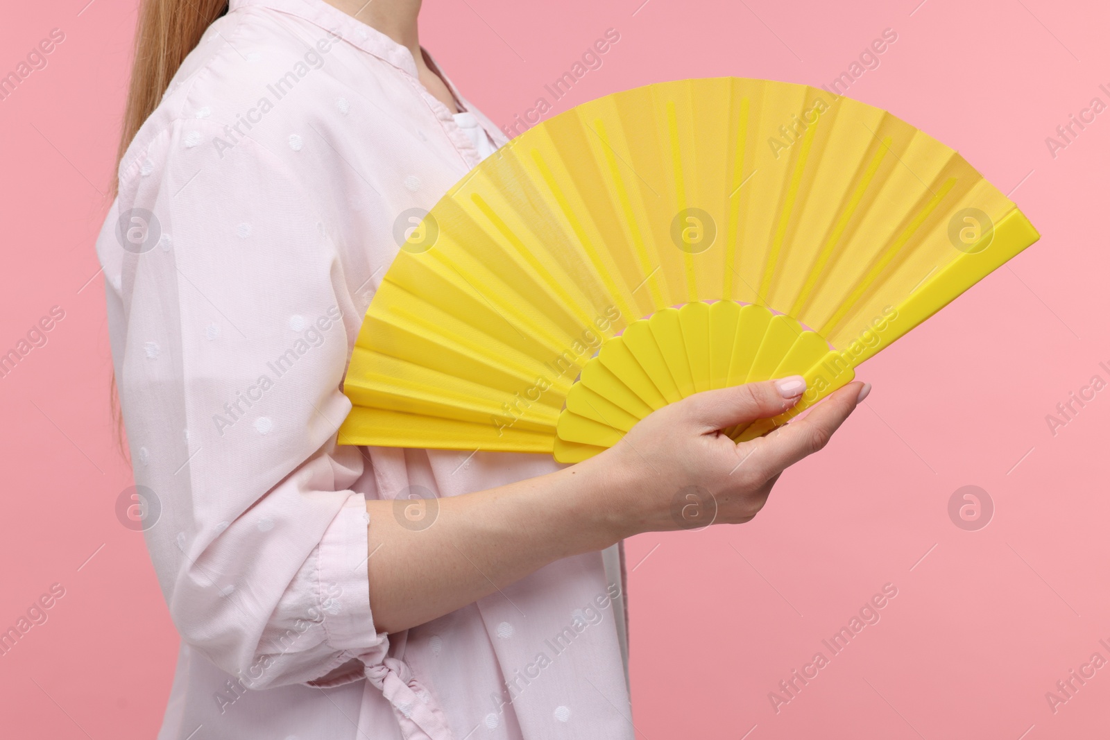 Photo of Woman with yellow hand fan on pink background, closeup