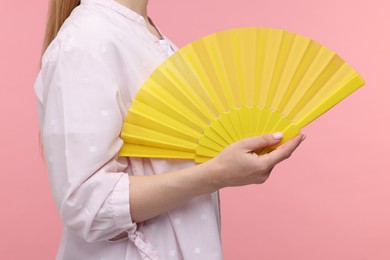 Woman with yellow hand fan on pink background, closeup