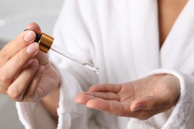 Photo of Woman applying cosmetic serum onto her hand on light background, closeup