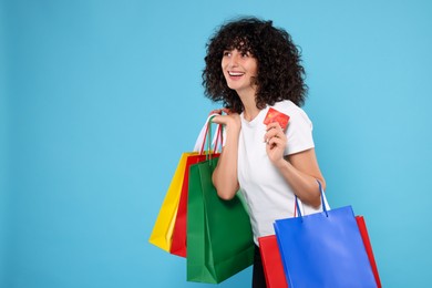 Photo of Happy young woman with shopping bags and credit cards on light blue background. Space for text