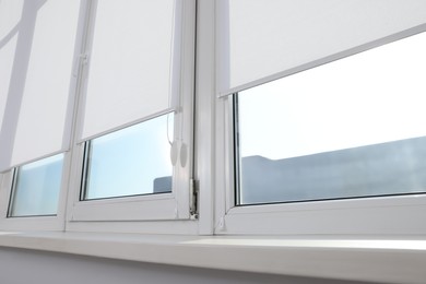 Photo of Large window with white roller blinds indoors