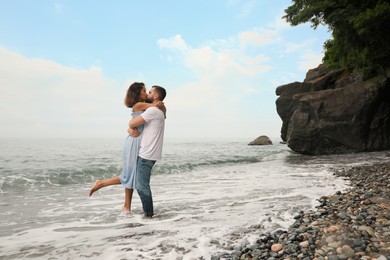 Photo of Young couple kissing on beach near sea, space for text