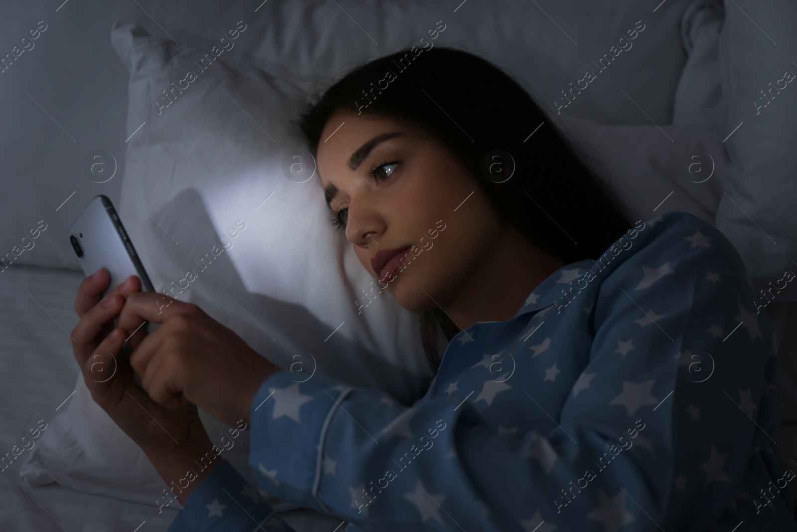 Photo of Young woman using mobile phone in dark bedroom