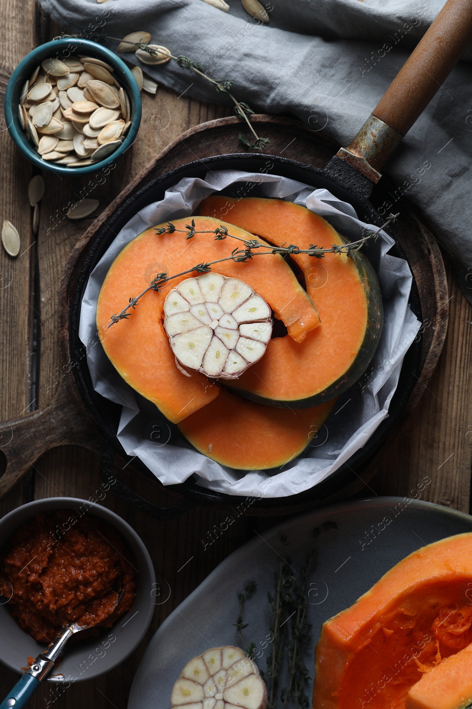 Photo of Fresh pumpkin slices with aromatic thyme and garlic in frying pan on wooden table, flat lay