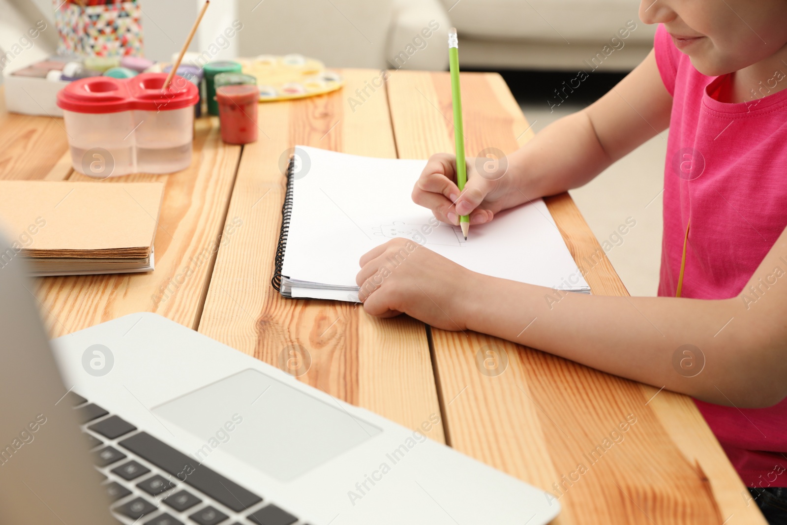 Photo of Little girl drawing on paper with pencil at online lesson indoors, closeup. Distance learning