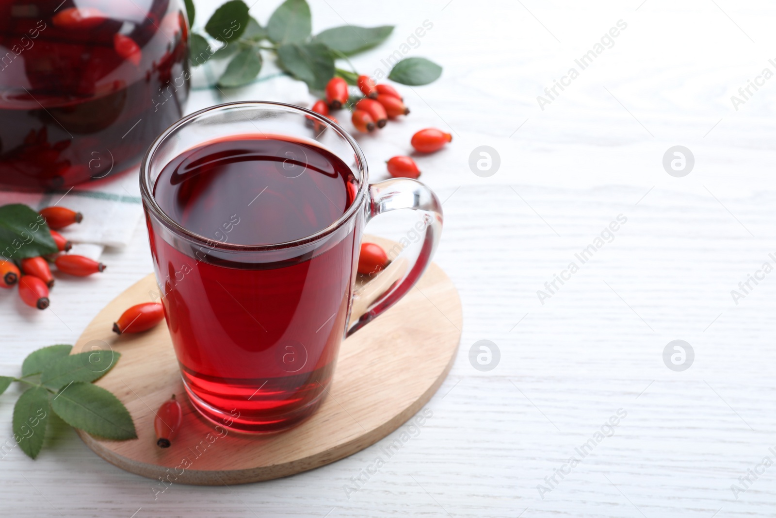 Photo of Aromatic rose hip tea and fresh berries on white wooden table, space for text