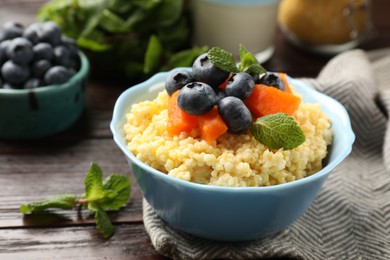 Photo of Tasty millet porridge with blueberries, pumpkin and mint in bowl on wooden table, closeup