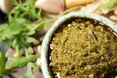 Photo of Bowl of tasty arugula pesto on table, closeup