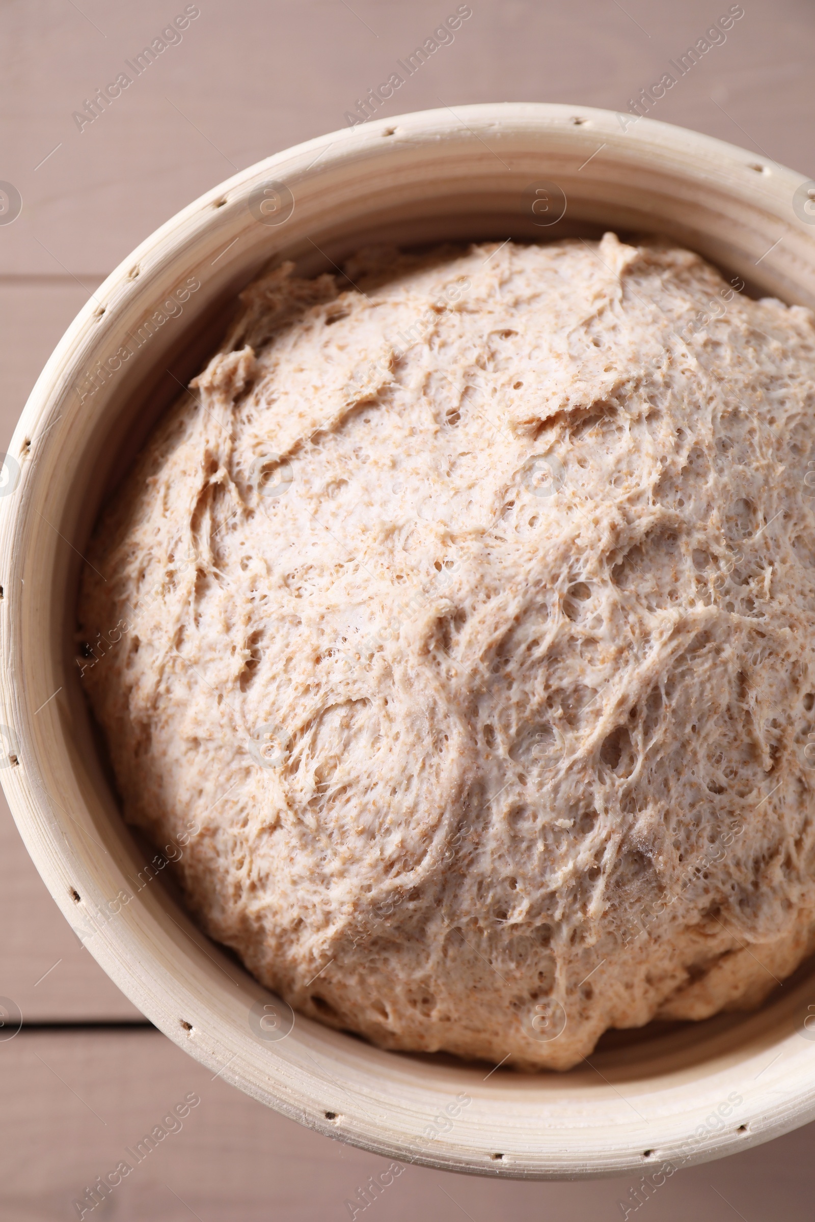 Photo of Fresh sourdough in proofing basket on wooden table, top view