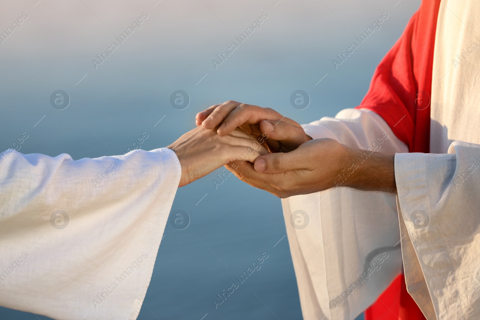 Photo of Jesus Christ holding woman's hand near water outdoors, closeup