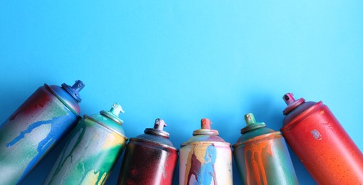 Photo of Many spray paint cans on light blue background, flat lay. Space for text