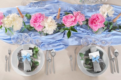 Photo of Beautiful table setting. Plates with greeting cards, napkins and branches near glasses, peonies, burning candles and cutlery on table, top view