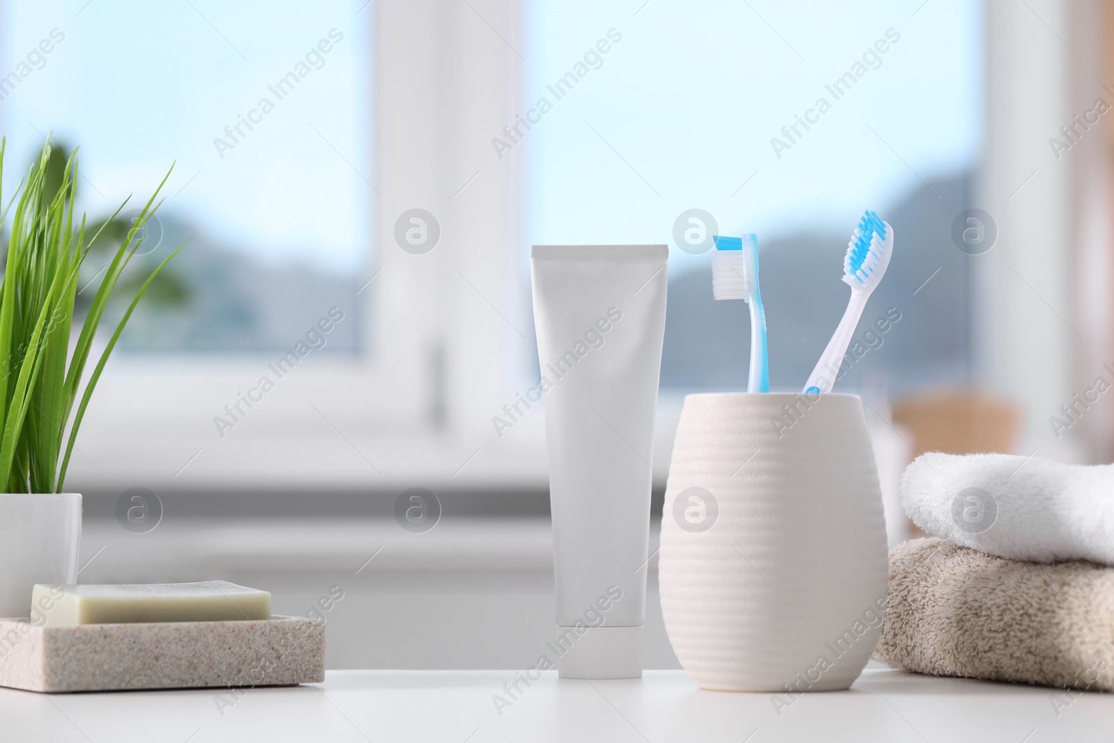 Photo of Plastic toothbrushes in holder, toothpaste, soap bar and towels on white table indoors