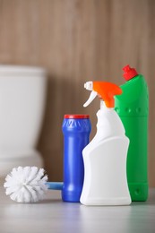 Photo of Bottles of cleaning products and toilet brush on table indoors