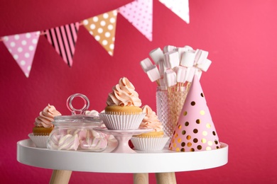 Table with party hat, cupcake and other sweets on burgundy background. Candy bar