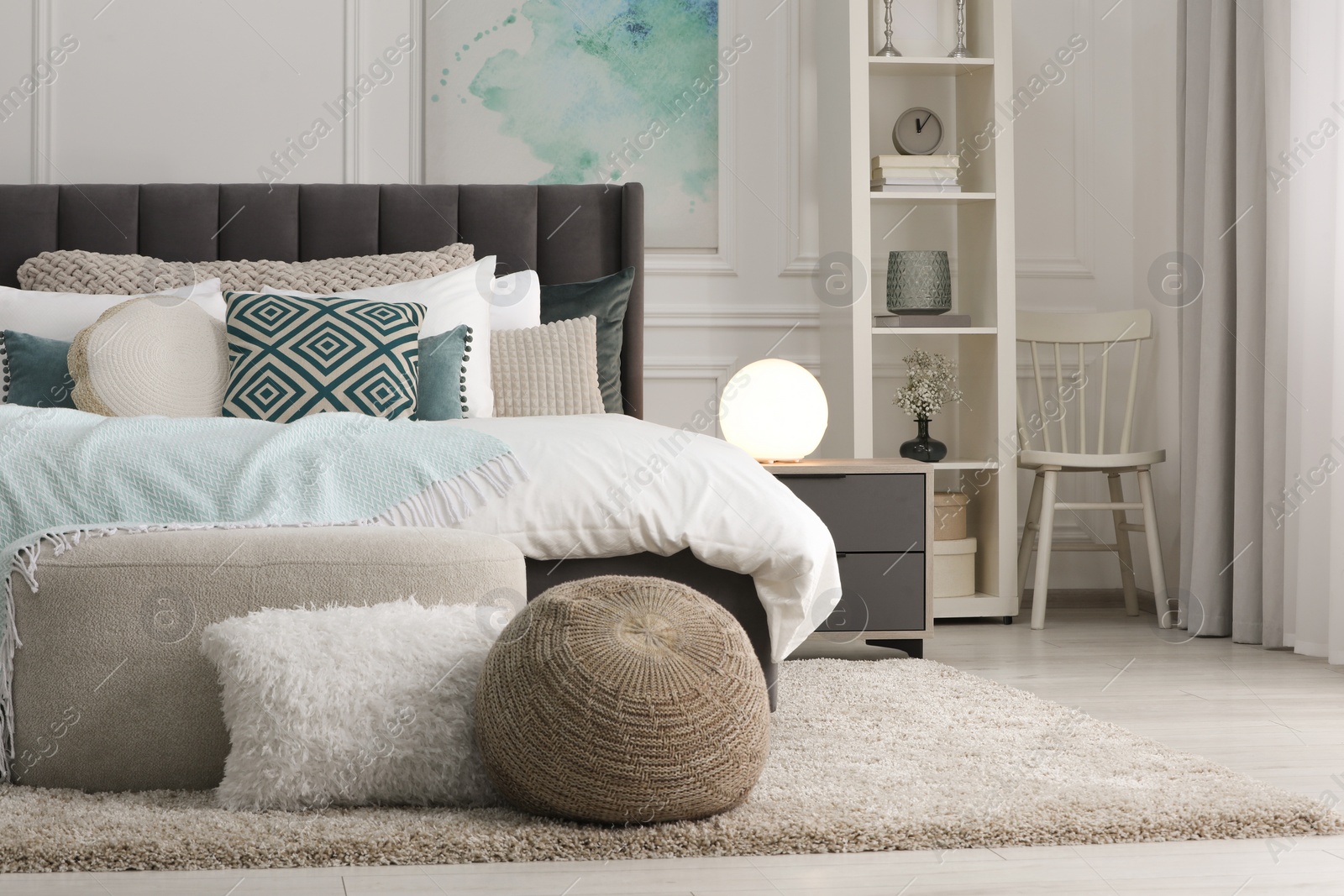 Photo of Stylish light bedroom interior with large comfortable bed, shelving unit and bedside table