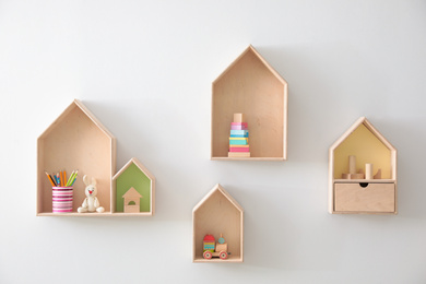 Different house shaped shelves with toys on white wall. Interior design