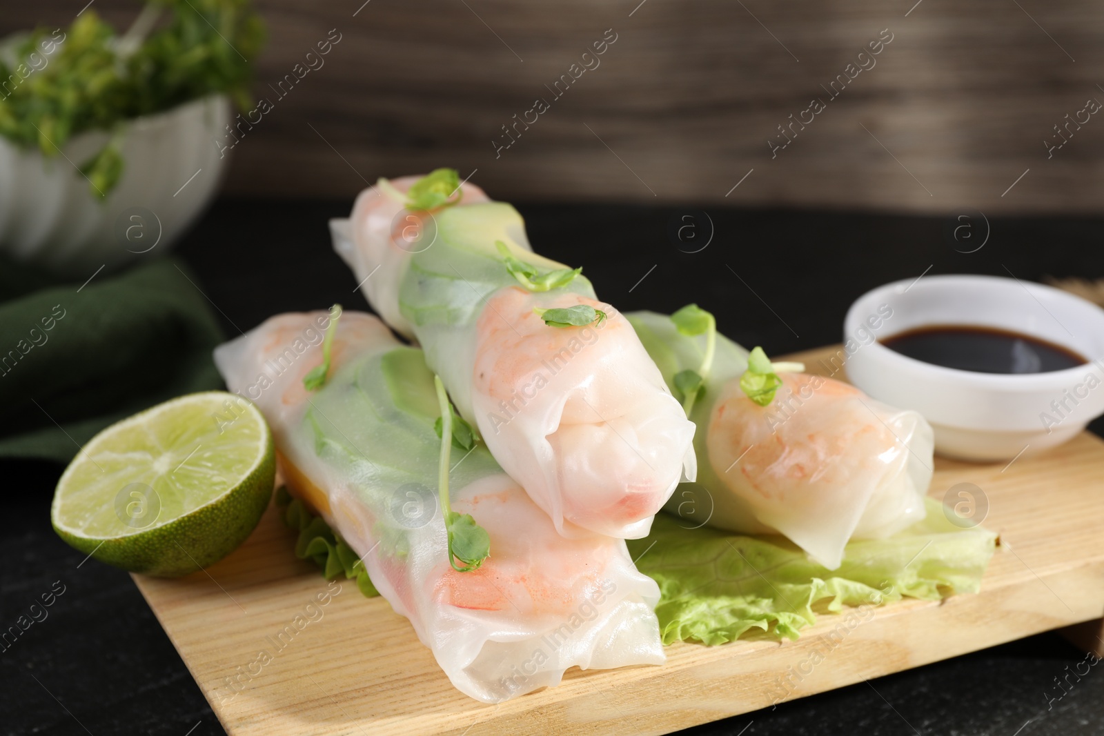 Photo of Delicious spring rolls, lettuce, lime and soy sauce on black table, closeup